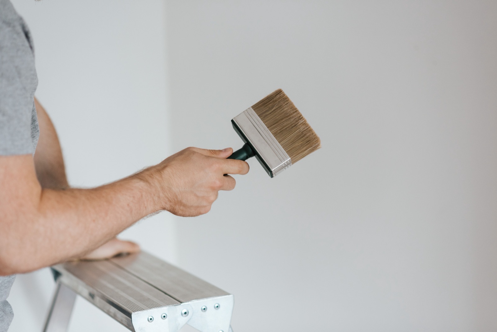 A wide brush in hand, ready to brush out a sample color on the wall